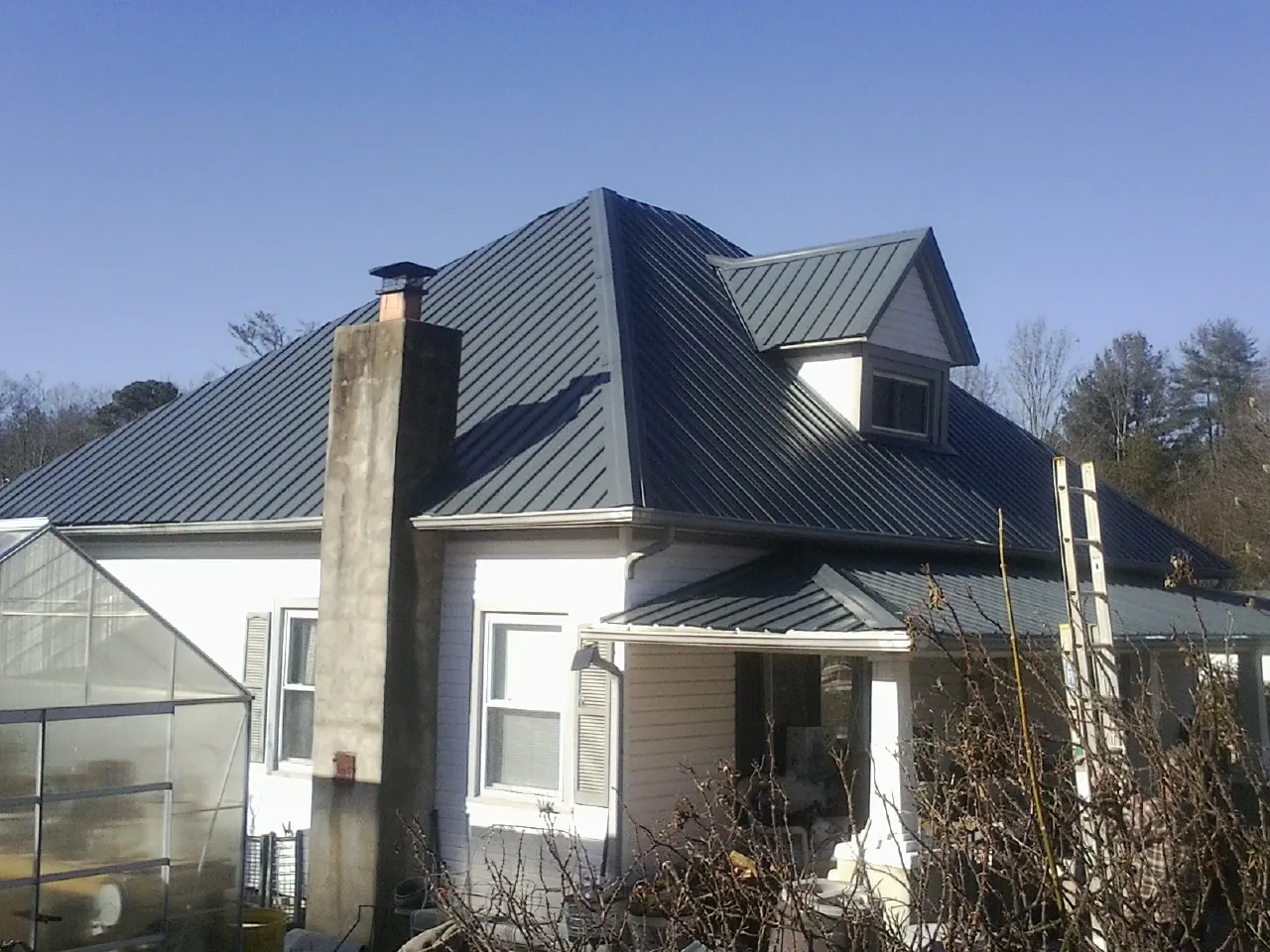 Dark blue standing seam metal roof on a white farmhouse with dormer — Slate & Tile Roof Repair by Roofing Brothers in Beallsville
