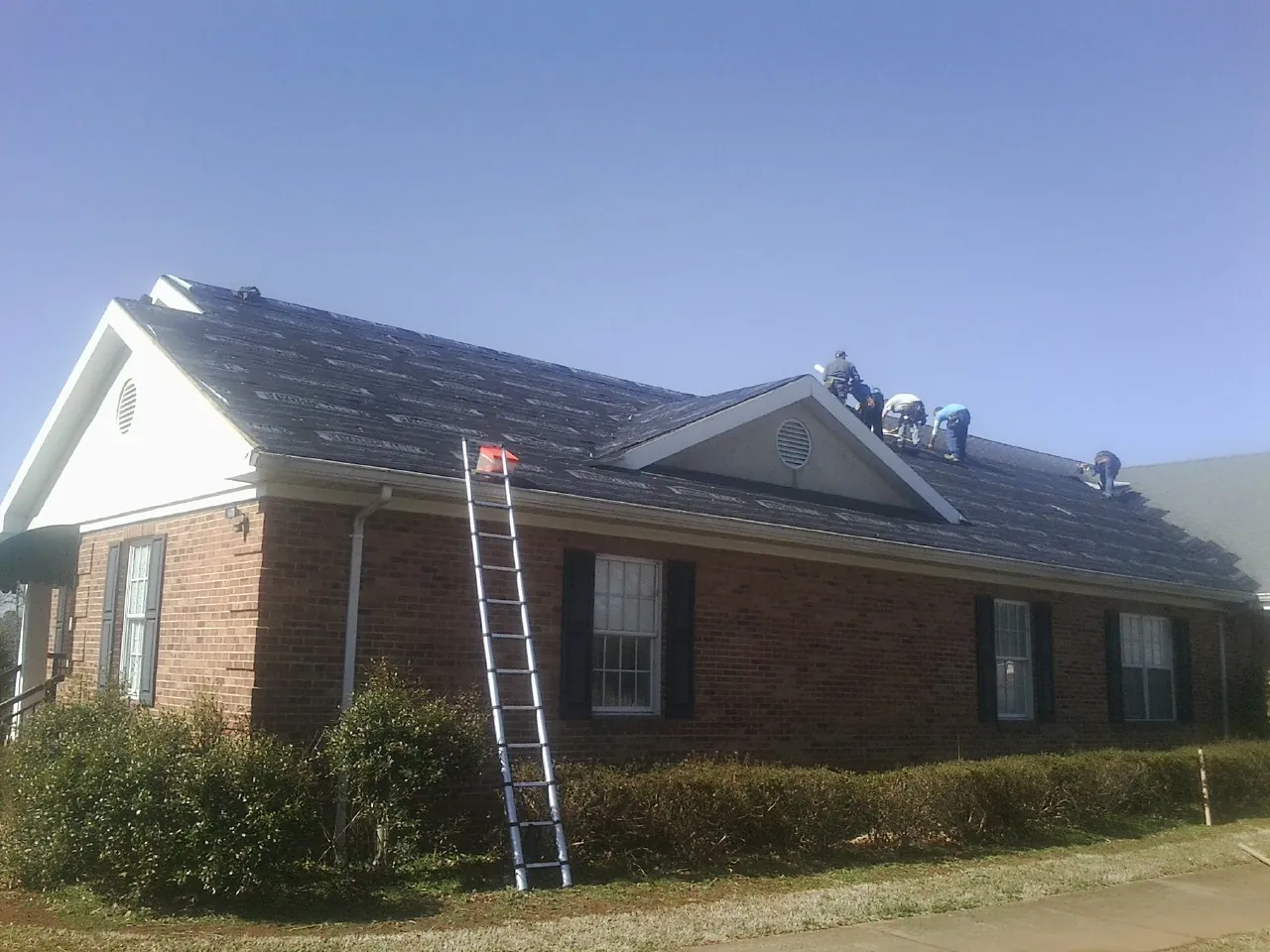 Crew tearing shingles off a brick ranch roof with a ladder set — Metal Roof Repair work by our crew in Beallsville