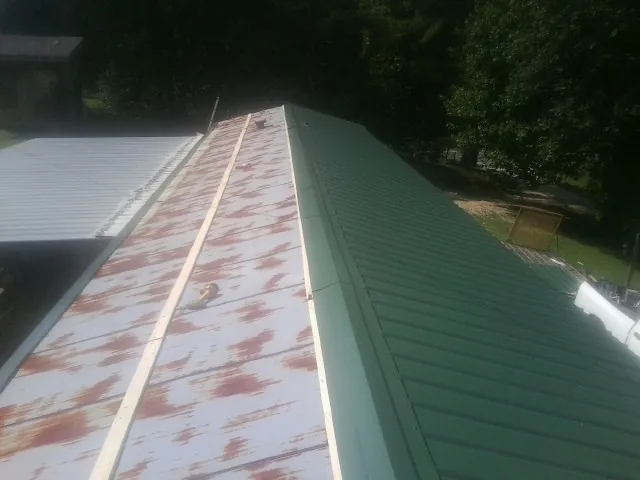 Old rusted panels beside newly installed green metal roofing — Wind Damage Roof Repair by Roofing Brothers in Beallsville