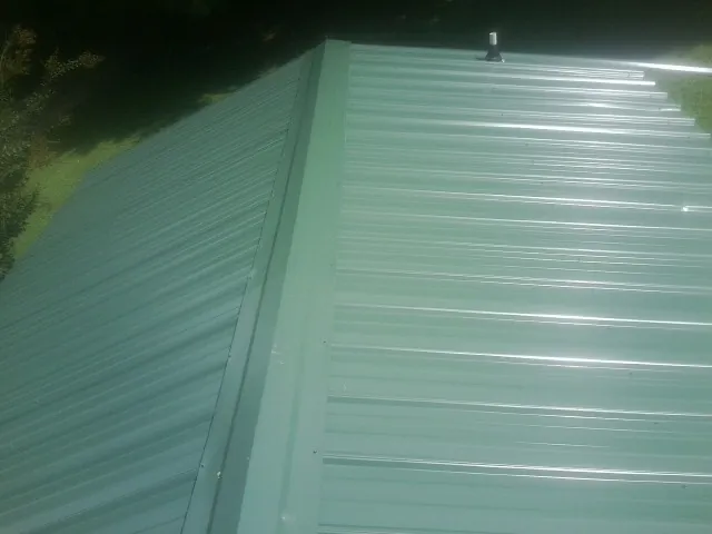 New green metal panels meeting at the ridge of a roof — Flat Roof Repair work by our crew in Beallsville